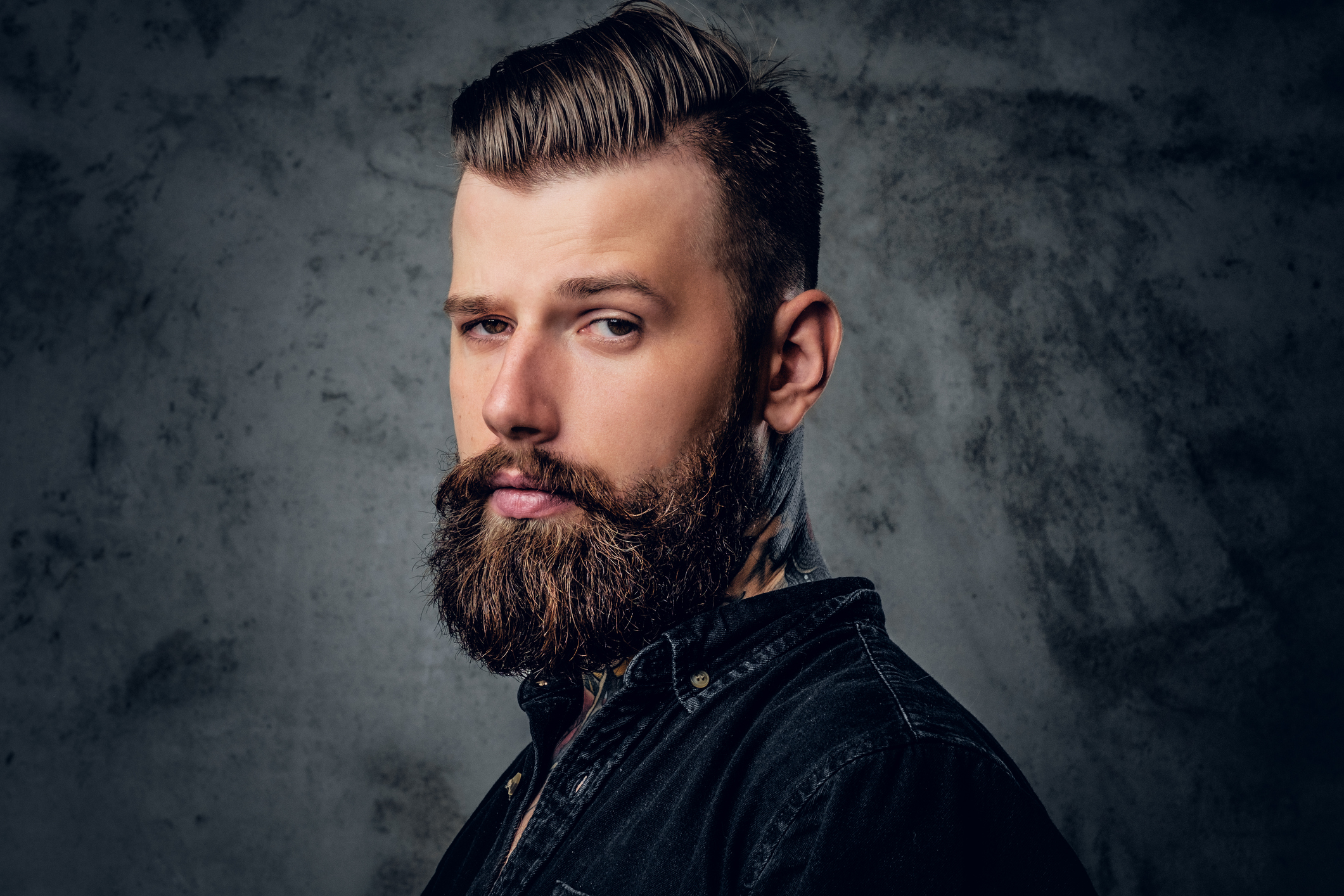 Portrait of bearded male in black shirt with tattoo on his neck.